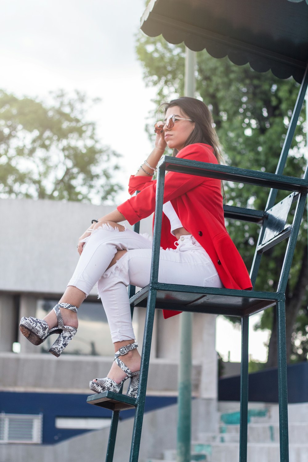 woman in white pants and red blazer sitting on chair with canopy