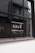A window with black framing has the word 'SALE' written in bold, white capital letters on its glass. The background shows a blurred interior and exterior environment, possibly of a store or commercial building.