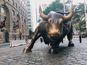 A sleek bull statue overlooking a bustling city skyline at sunrise, symbolizing strength in finance.
