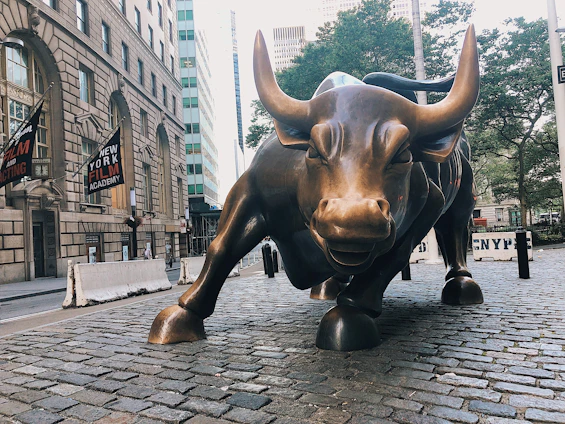 A sleek bull statue overlooking a bustling city skyline at sunrise, symbolizing strength in finance.