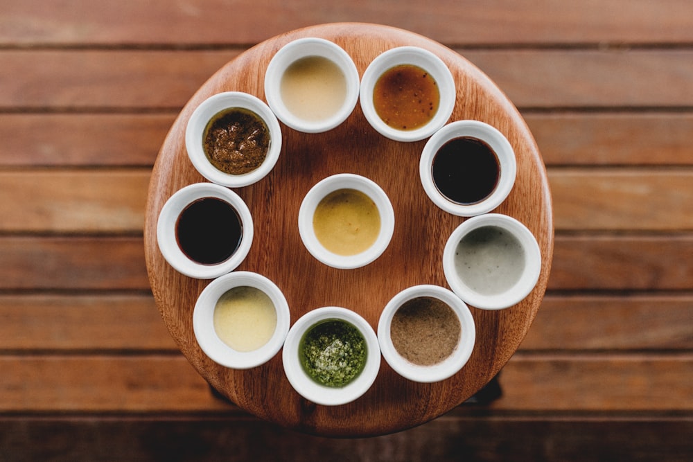 una mesa de madera cubierta con tazas blancas rellenas de salsas