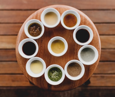 a wooden table topped with white cups filled with sauces