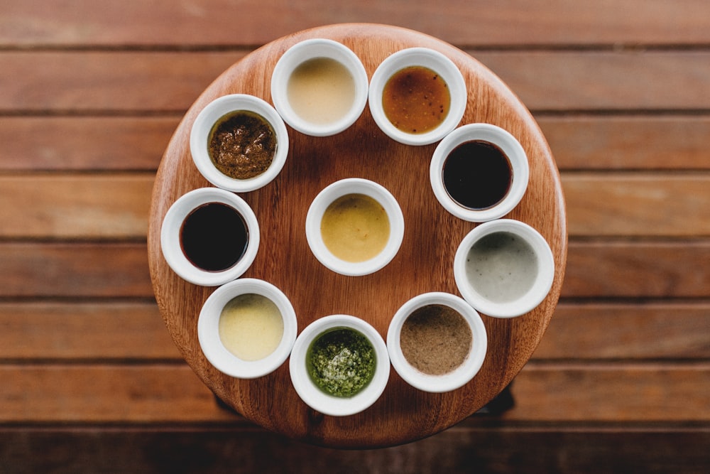 a wooden table topped with white cups filled with sauces