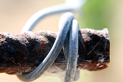 A close-up of a rusty metal rod wrapped with silver wire, surrounded by the texture of the rust and a few faint spiderweb threads.