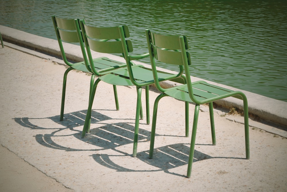 three green metal chairs near body of water