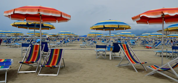 A sunny Oak Island beach scene with colorful umbrellas, chairs, and coolers set up near the shore.