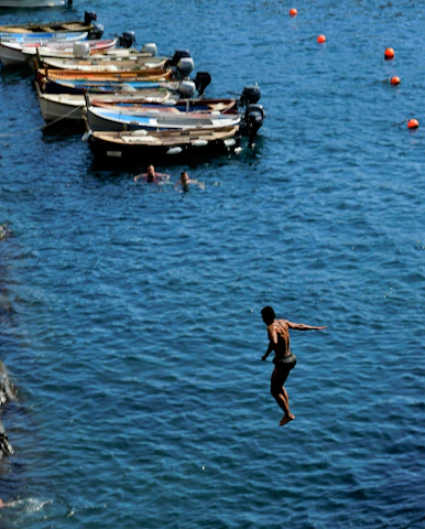 Athlete preparing to dive into deep blue waters with rocky coastline in background.