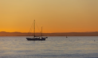 A sailboat gently cruising on calm waters with a vibrant orange and pink sunset over Banderas Bay.
