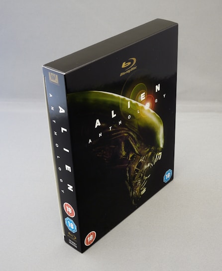 A Blu-ray box set of 'Alien Anthology'. The cover is predominantly dark with a striking image of an alien creature in profile, highlighted with greenish hues. The title 'ALIEN ANTHOLOGY' is prominently displayed across the cover in white lettering. Age ratings are visible on the lower front cover.