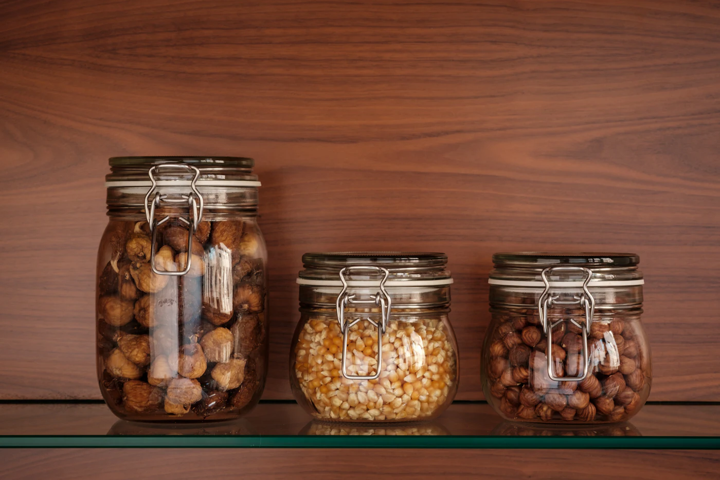 Trois bocaux en verre réutilisables remplis de figues sèches, maïs et noisettes