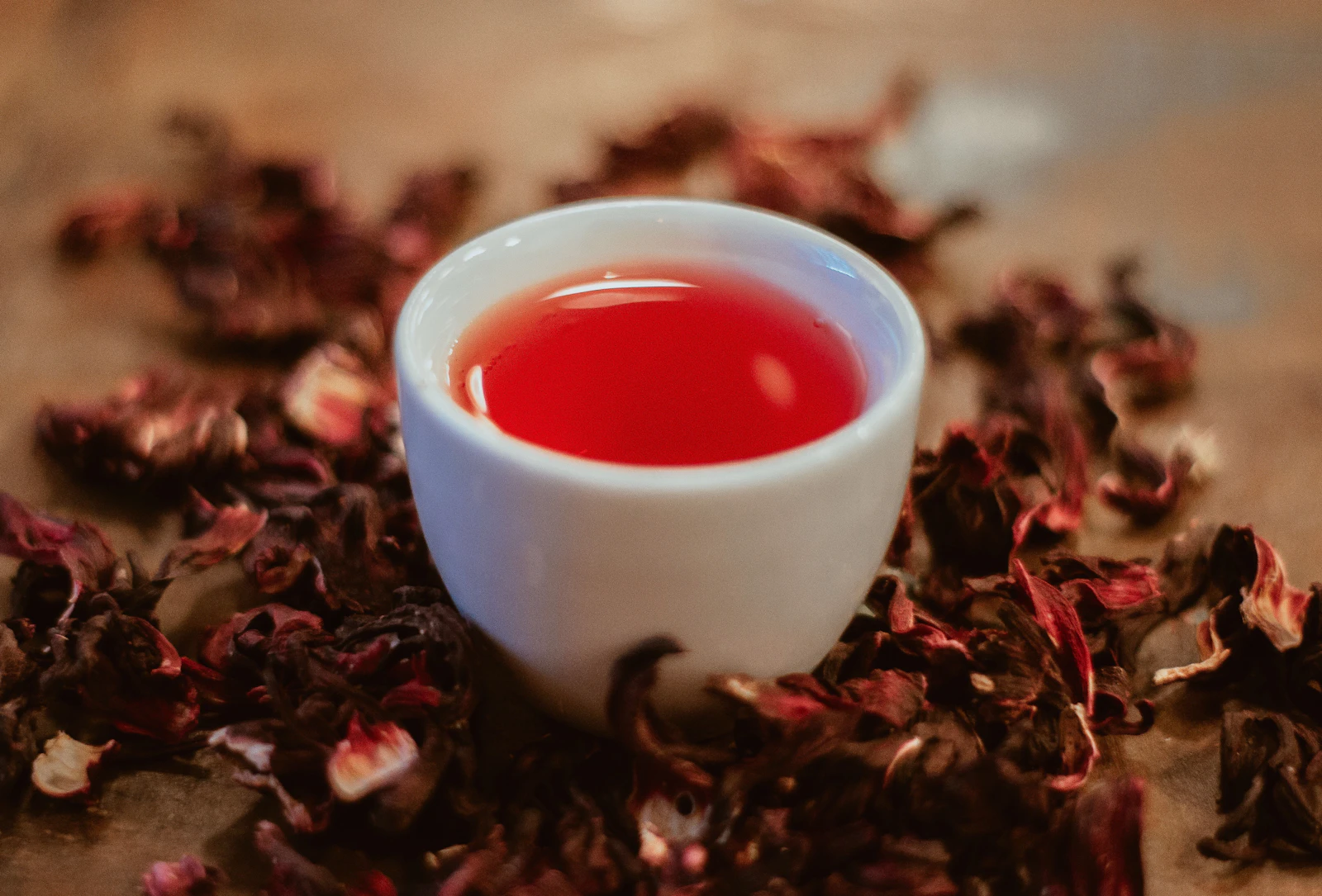 A cup of bright red hibiscus tea surrounded by dried hibiscus flowers