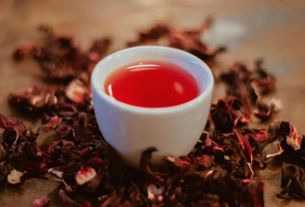 A white cup of ruby-red hibiscus tea encircled by whole dried hibiscus flowers