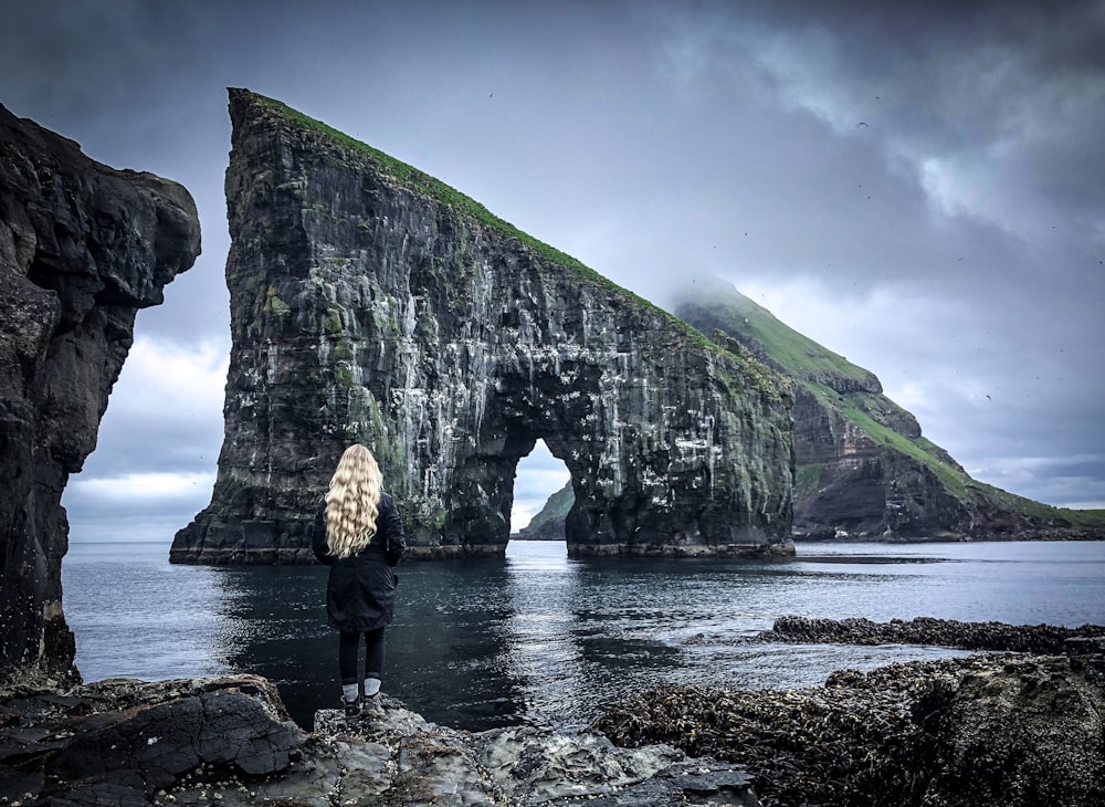 woman standing near body of water near rock formation