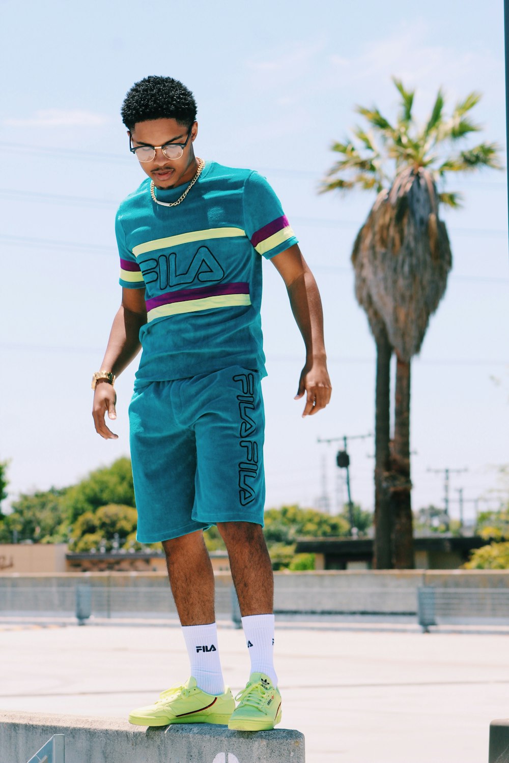 man in teal Fila T-shirt and shirts standing near palm tree in park