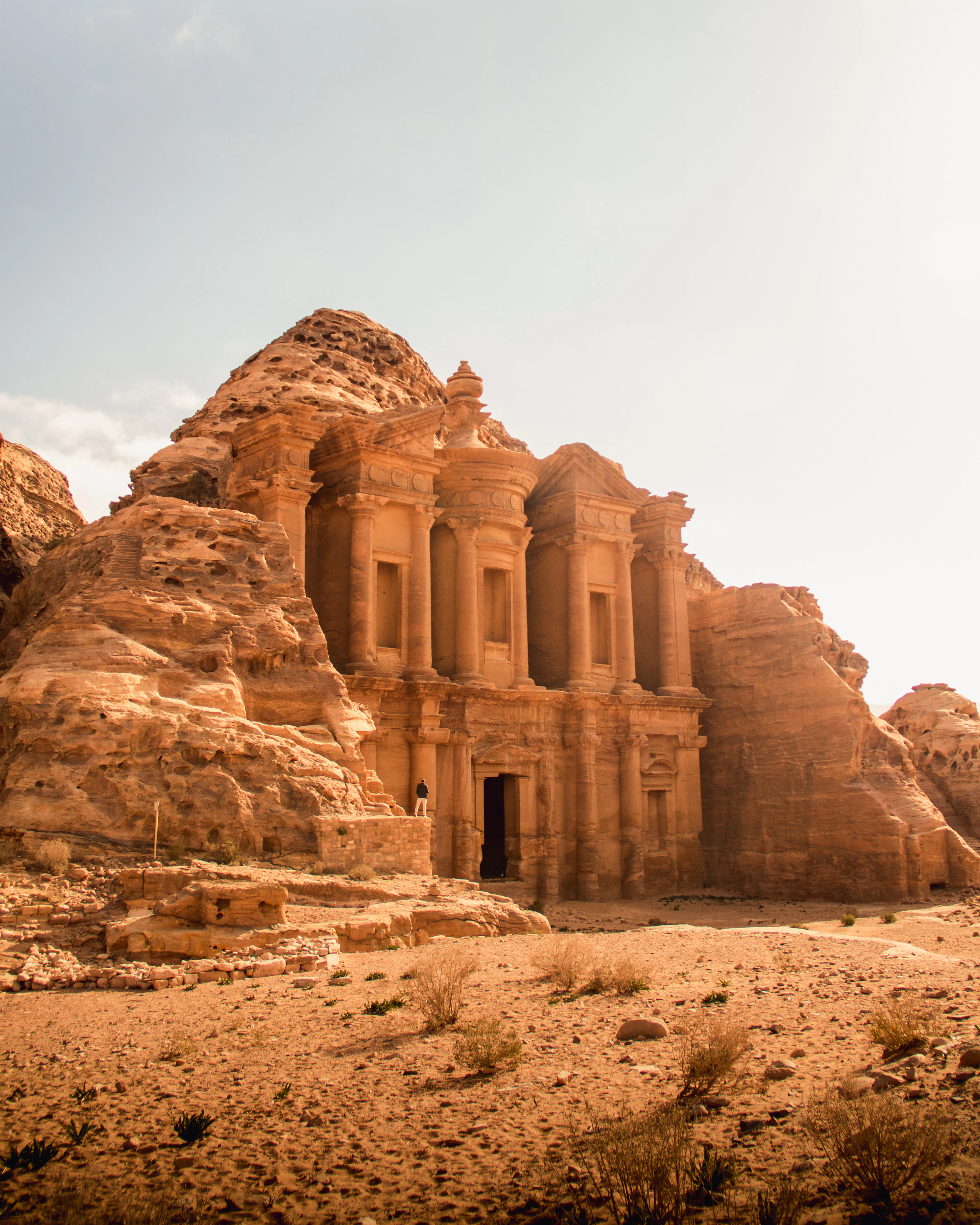 Ad Deir, the Monastery at Petra, its huge columned facade carved straight into honey-coloured sandstone above an empty sandy forecourt.