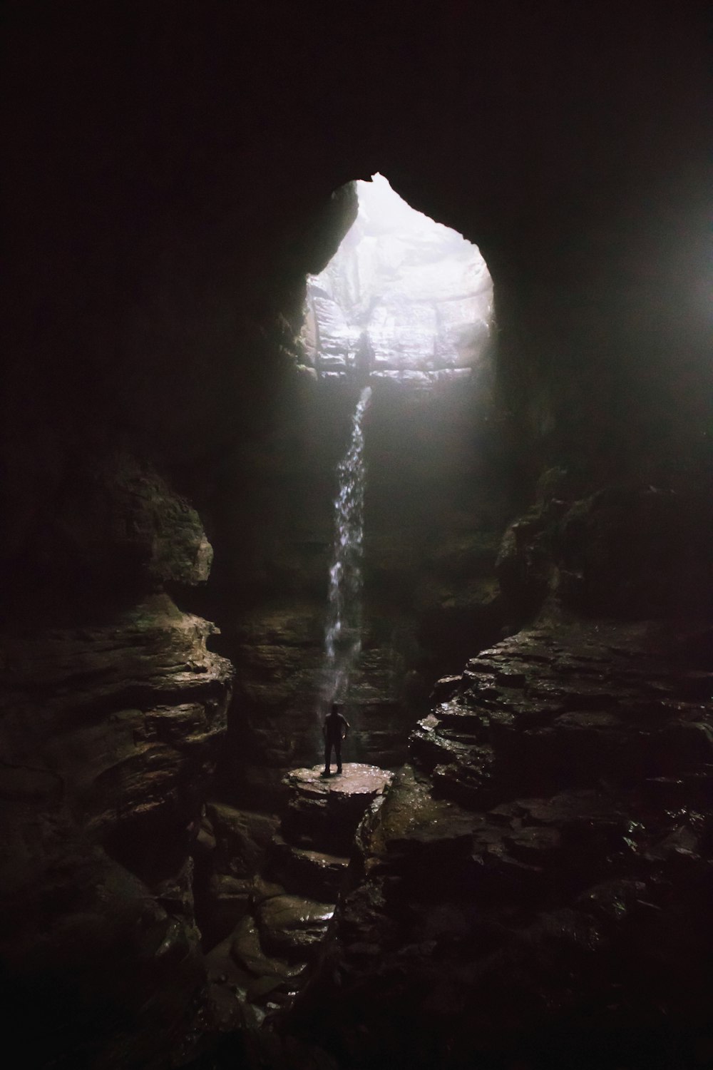 man standing in cave with water falls