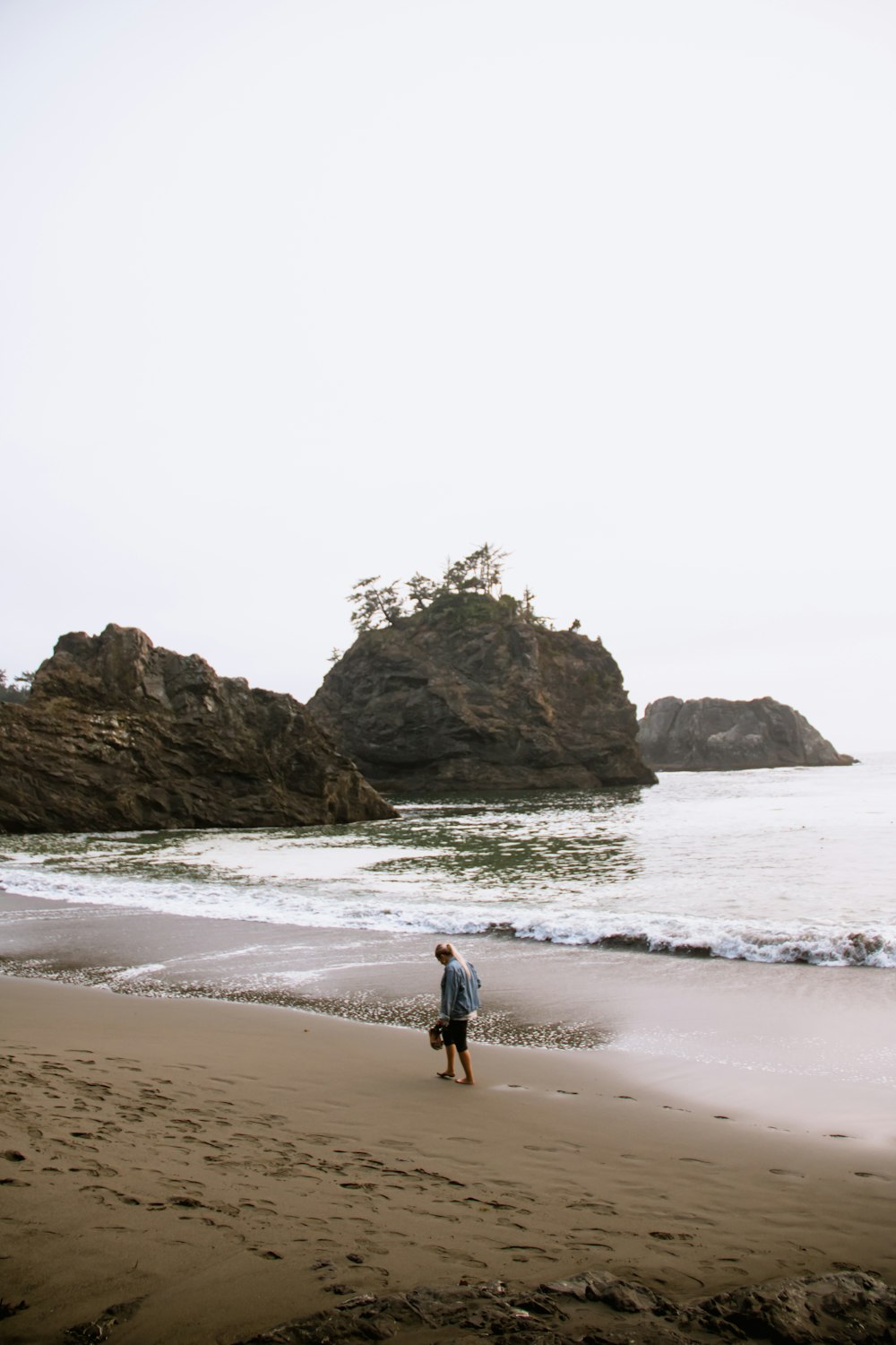 man walking on seashore under white sky