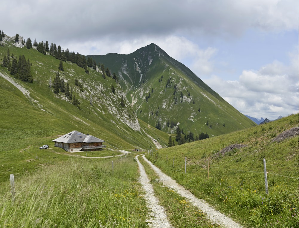 casa de madera marrón en campo verde que ve la montaña bajo cielos blancos y azules