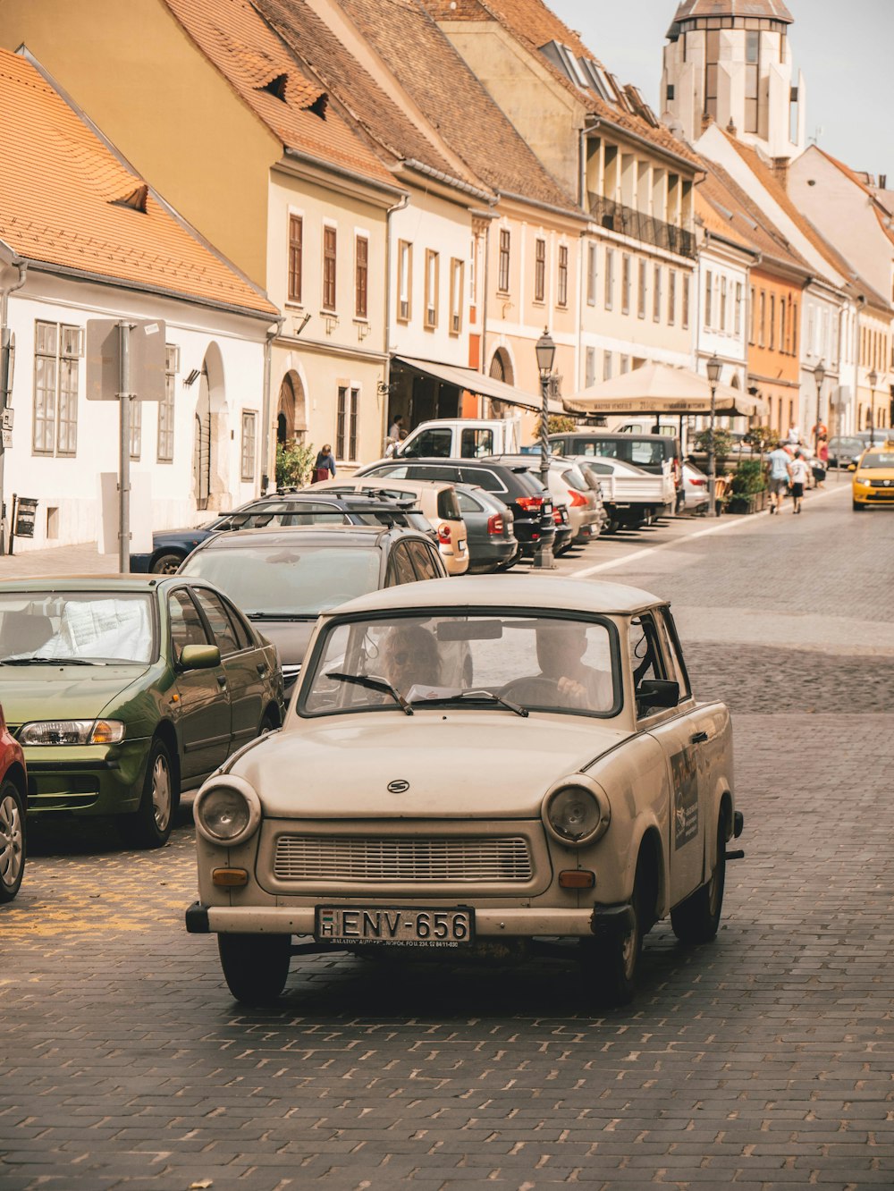 car on the road near cars parked at the side and buildings during day