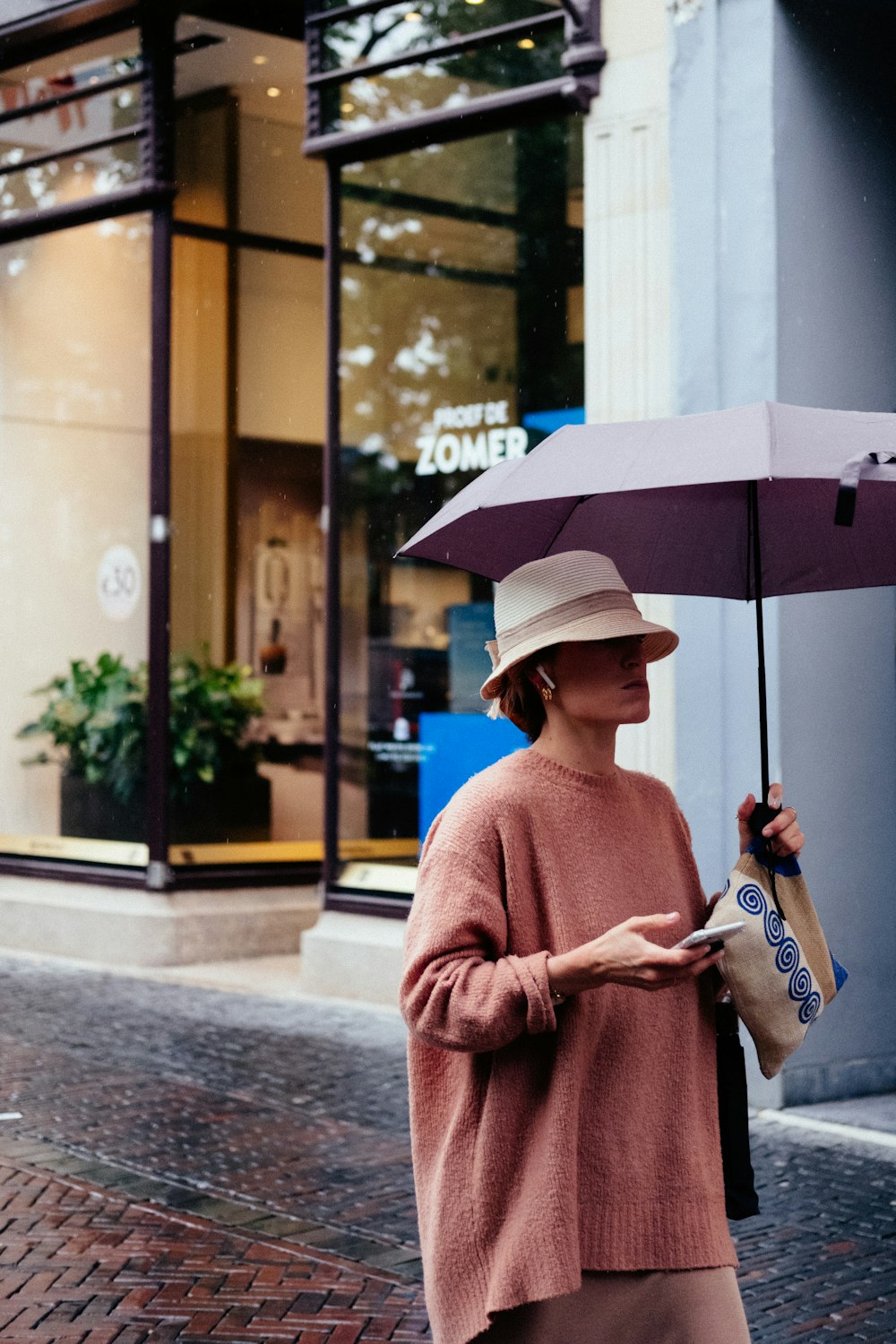 woman holding smartphone and umbrella while walking near building