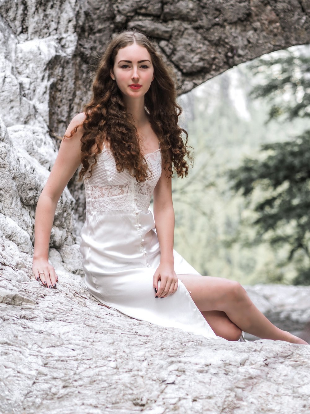 岩の上に座っている白いボタンアップドレスを着た笑顔の女性