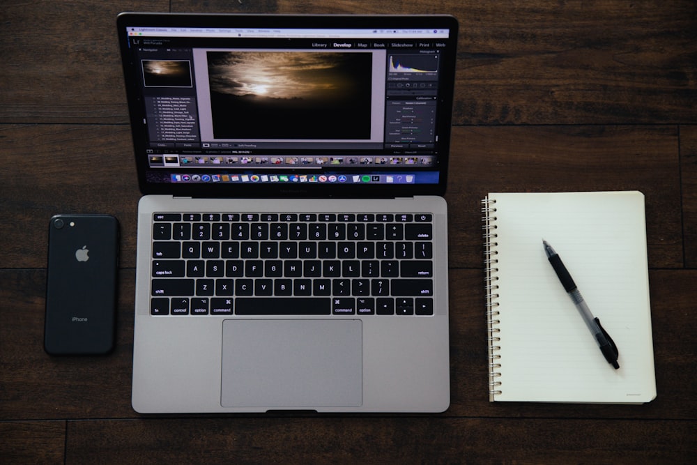 MacBook Pro near spiral notebook with pen on top and black iPhone 8