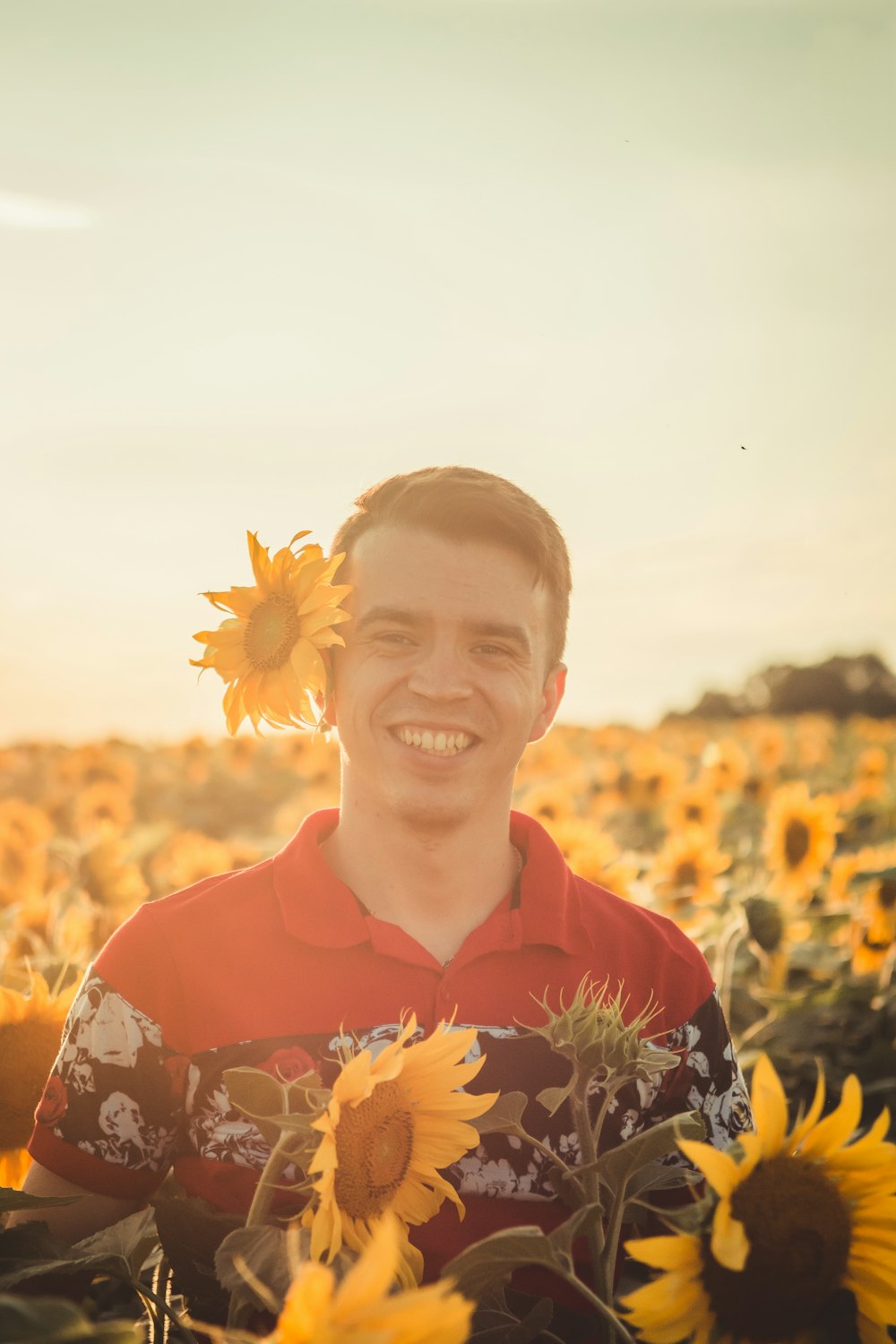 man with sunflower on ear standing and smiling