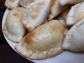 Several golden-brown baked pastries are neatly arranged on a white plate. The pastries have a semi-circular shape with crimped edges, showing a glossy, evenly baked surface.