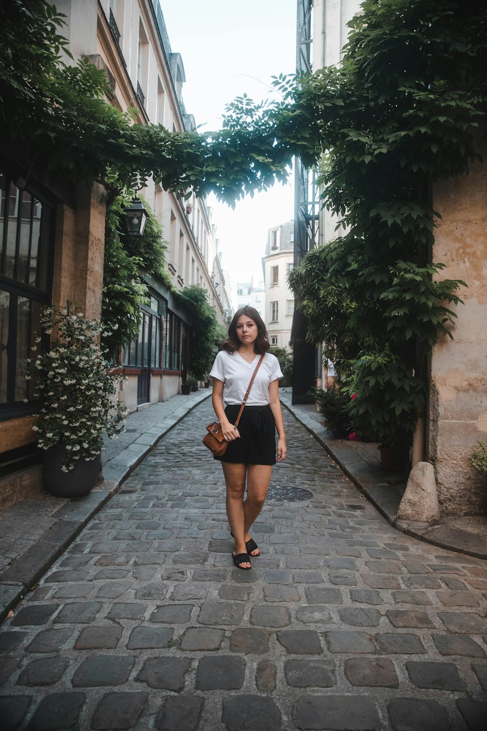 woman standing on pavement in between buildings during daytime