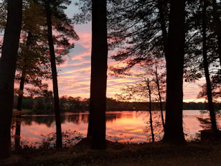 Wide shot of a serene lakeside at sunset with pastel colors reflecting on the water.