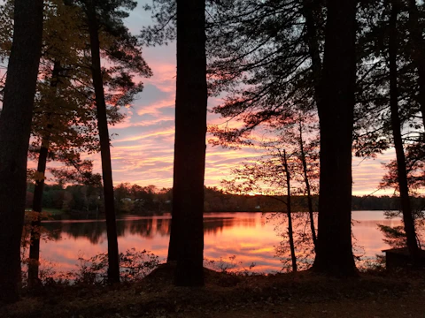 Wide shot of a serene lakeside at sunset with pastel colors reflecting on the water.