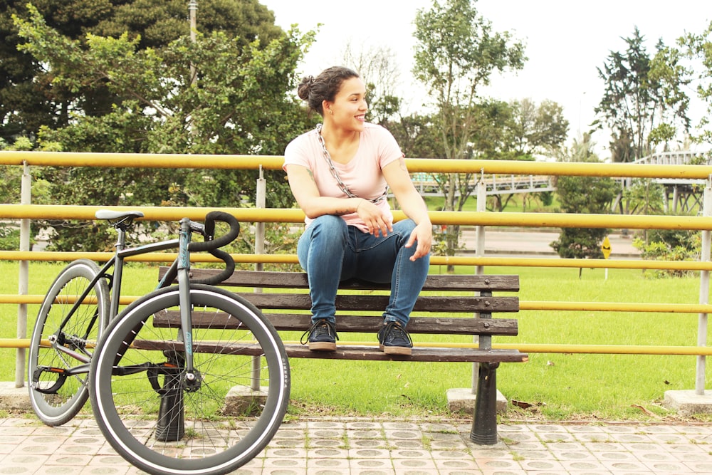 woman wearing blue jeans sitting on brown outdoor bench