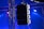A set of large speakers is suspended from a metal truss structure. Vibrant lights in shades of blue and purple illuminate the scene, creating a dramatic effect. The setup appears to be part of a stage or concert venue, emphasizing professional sound equipment.