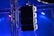 A set of large speakers is suspended from a metal truss structure. Vibrant lights in shades of blue and purple illuminate the scene, creating a dramatic effect. The setup appears to be part of a stage or concert venue, emphasizing professional sound equipment.