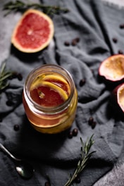 A vibrant jar of fermented lemons surrounded by fresh herbs and spices.