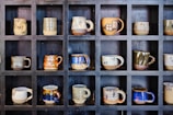 Set of functional ceramic mugs lined up on a wooden shelf, each with unique glaze patterns.