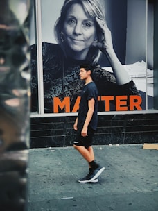 A young person in athletic wear walks along a city street in front of a large black-and-white advertisement featuring a woman with a thoughtful expression. The word 'MATTER' in bold orange letters is partially visible. The scene depicts an urban environment.