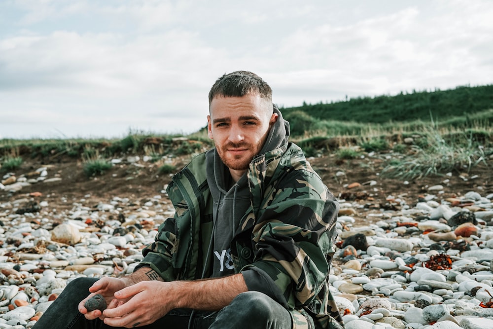 man wearing green and black camouflage jacket sitting across green hills