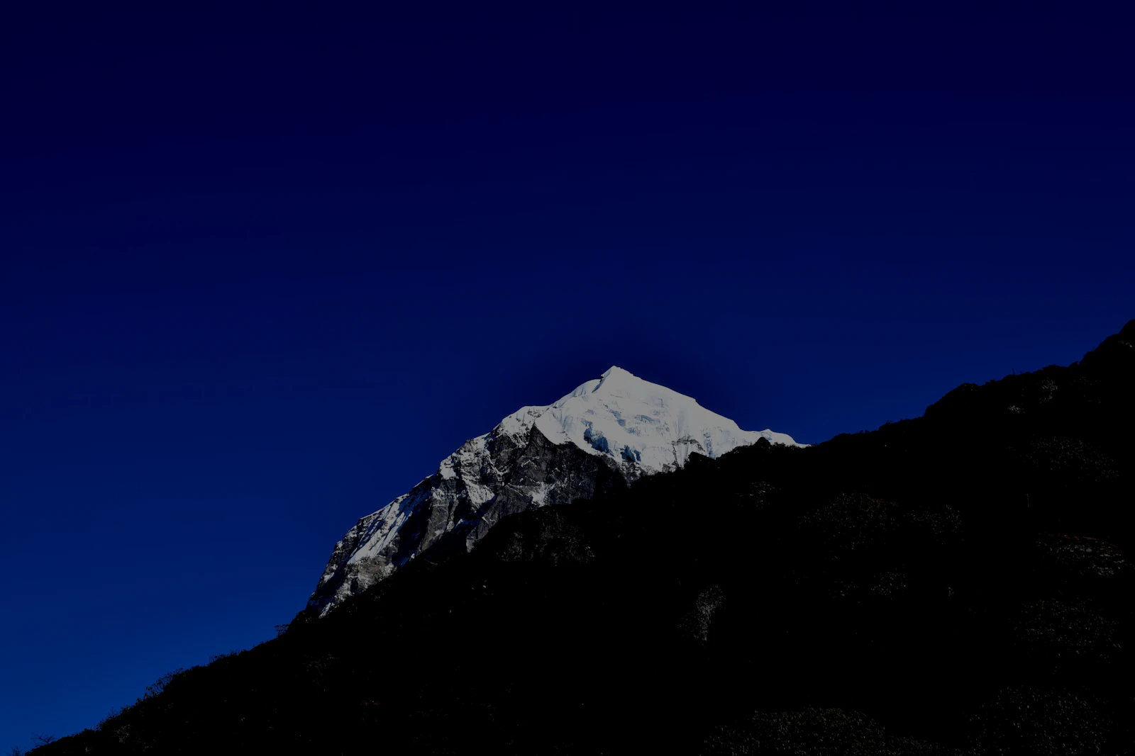 The snow summit of Pandim above a dark ridge under a deep blue evening sky, West Sikkim