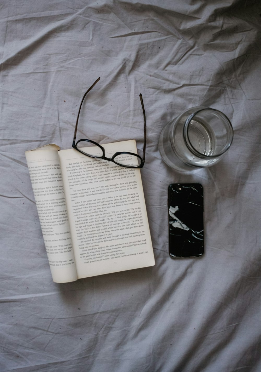 smartphone, opened book, eyeglasses, and drinking glass