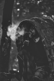 A person is seated in a rickshaw, exhaling smoke. The setting suggests a serene yet contemplative mood, with the individual partially covered by the rickshaw's canopy. The image is rendered in black and white, highlighting the texture and contrasts of the scene.