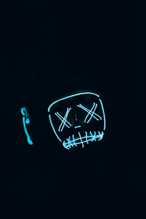 A dark, eerie setting with a glowing, stylized face mask that has Xs for eyes and a stitched mouth design, outlined in neon blue.
