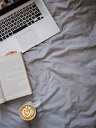 A cozy writing nook with a laptop, coffee cup, and stacks of books.