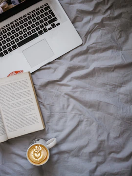 A cozy writing nook with a laptop, coffee cup, and stacks of books.