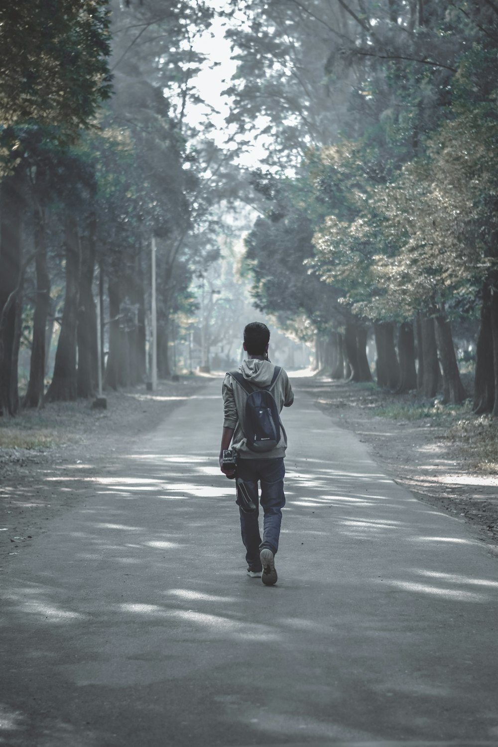 man in grey hooded jacket walking on grey concrete road