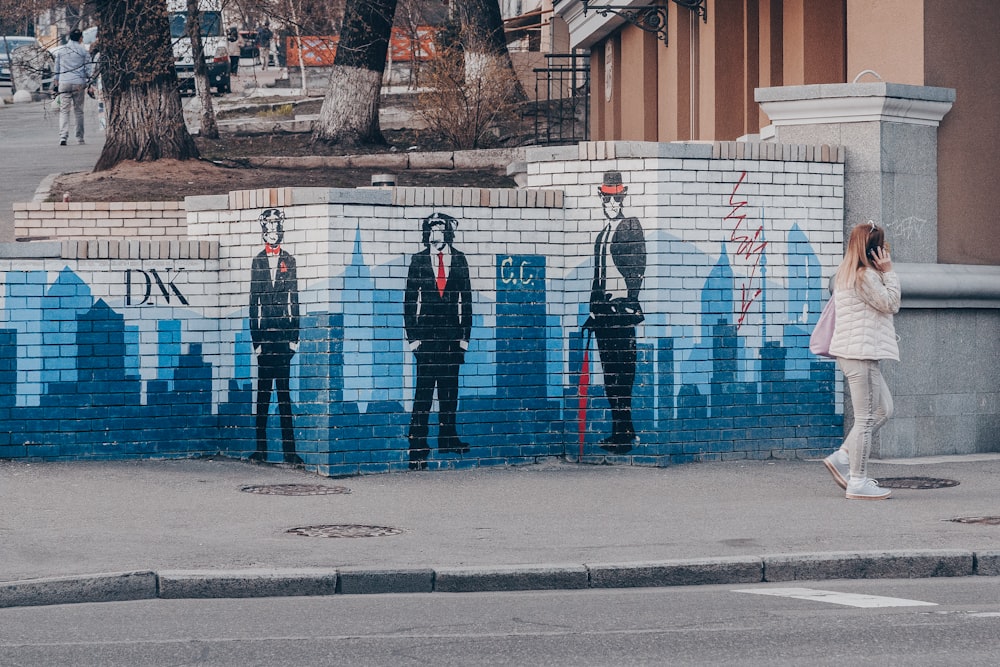 a woman standing in front of a wall with a mural of men in suits