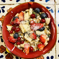 A colorful serving of crunchy muesli with dried fruits and seeds in a modern white bowl.