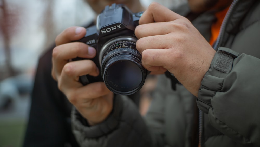 man in grey jacket holding Sony DSLR camera