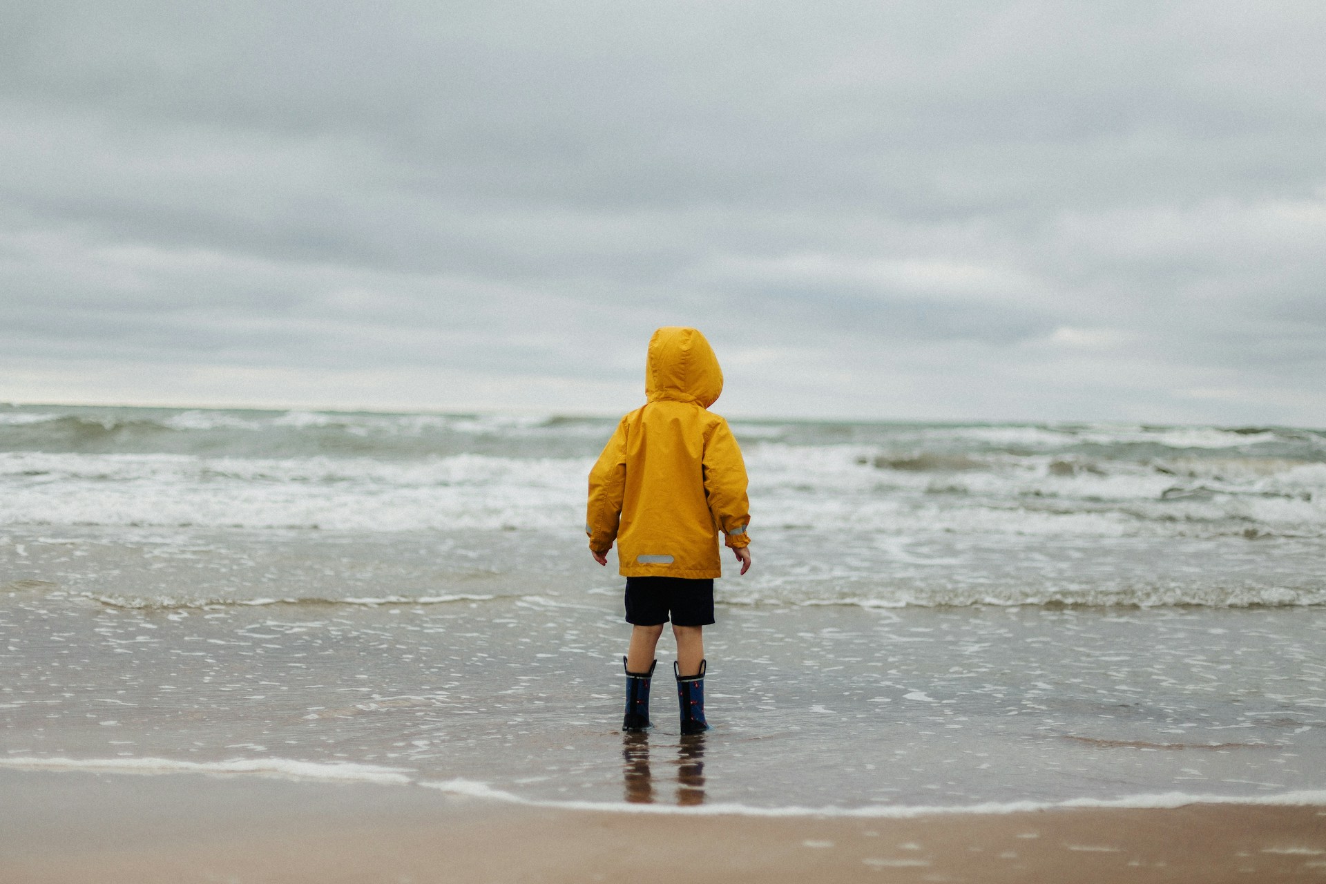 toddler wearing yellow hoodie and black shorts standing on seashore