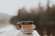 Steaming cup of coffee next to a tea pot on a wooden picnic table
